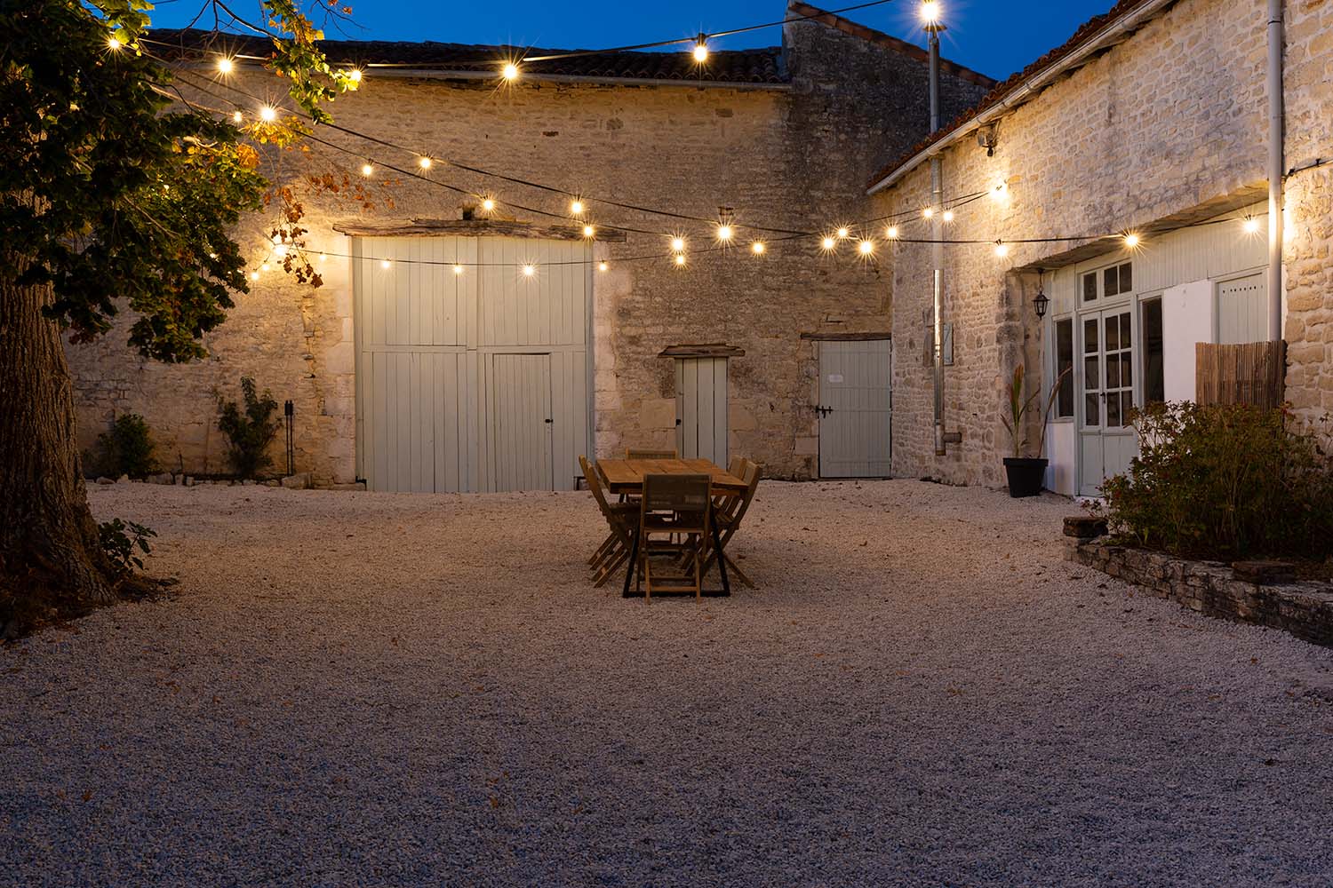 A table and chairs illuminated by festoon lights in the courtyard of a luxury self catering villa in France